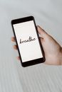 From above of crop unrecognizable person demonstrating cellphone with Breathe inscription above bed sheet