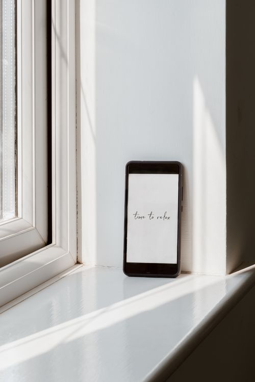 Free Modern cellphone with Time To Relax title on screen near window at home in sunlight Stock Photo