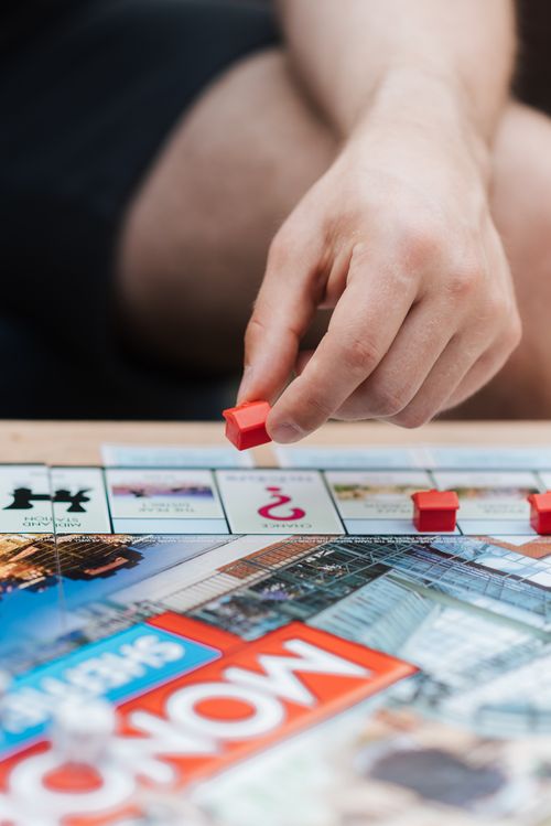 Free Crop anonymous male with artificial red house playing board game with illustration at desk in daytime Stock Photo