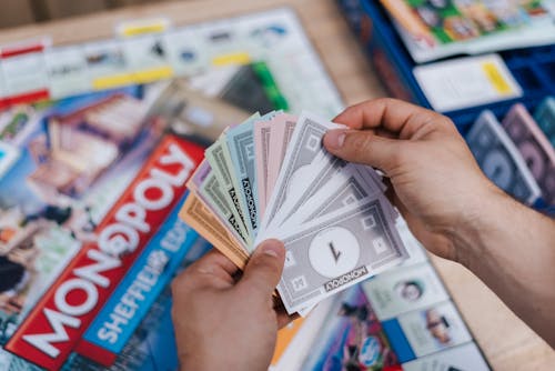 Free From above of crop anonymous man with set of game money playing Monopoly above board Stock Photo