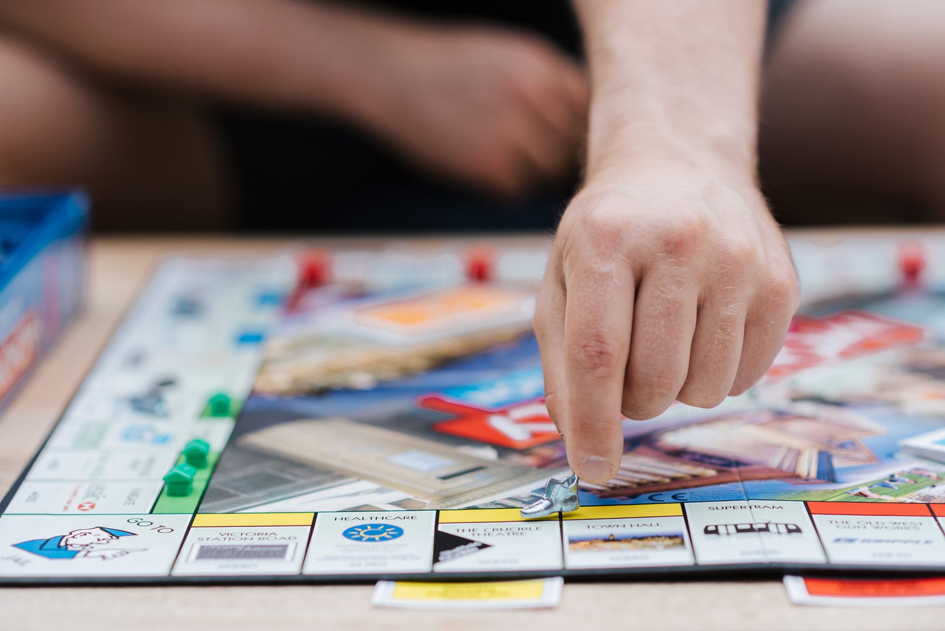 A person plays Monopoly, the famous board game, moving a piece across the board indoors.