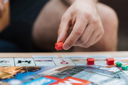 Free Crop unrecognizable man with artificial red house playing board game at table on weekend Stock Photo