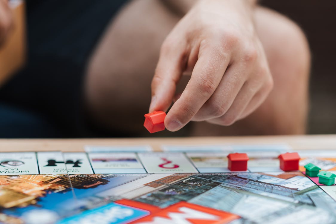 Crop unrecognizable man with artificial red house playing board game at table on weekend