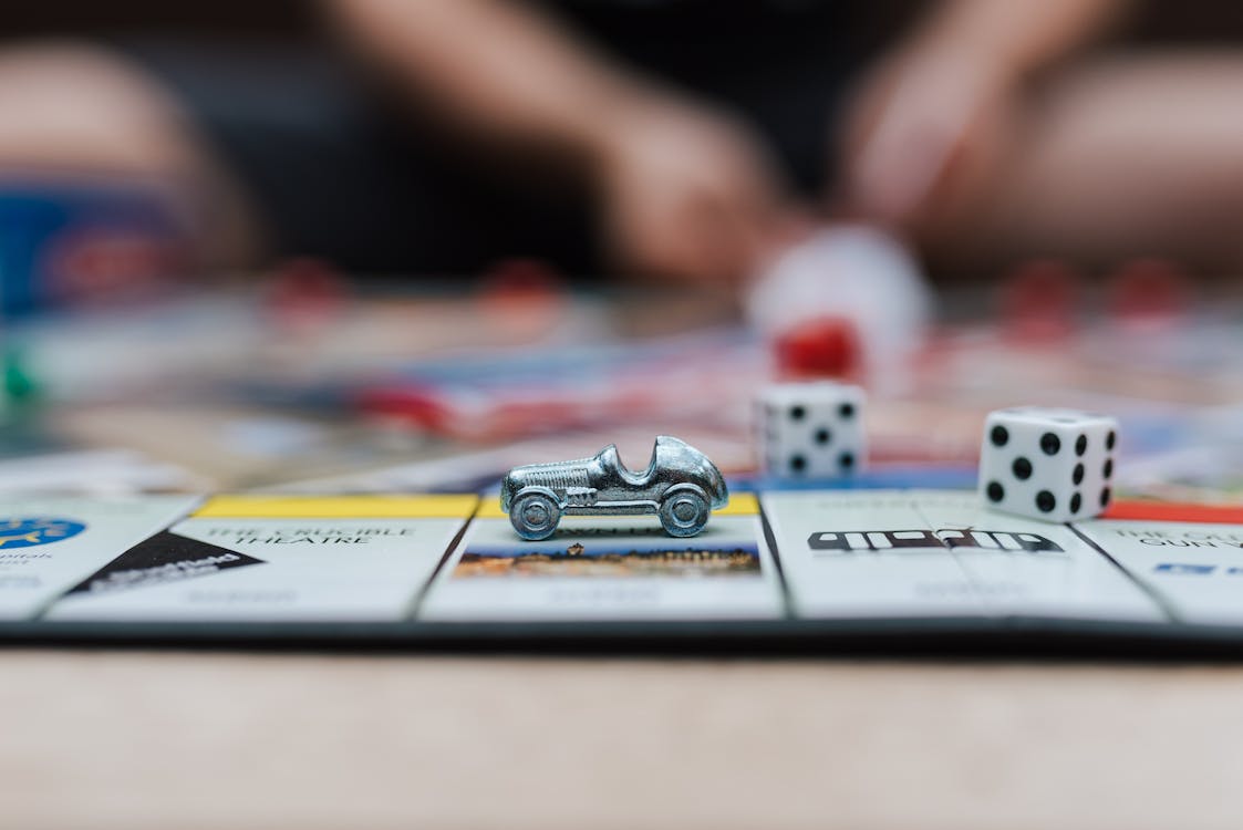 Free Crop anonymous man playing Monopoly at table with small plastic auto and similar dices Stock Photo