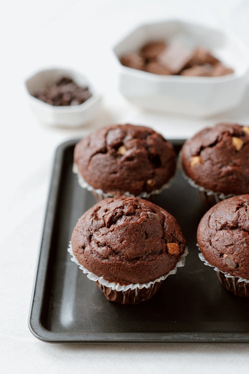 From above of sweet chocolate muffins in white paper cups arranged on tray in kitchen