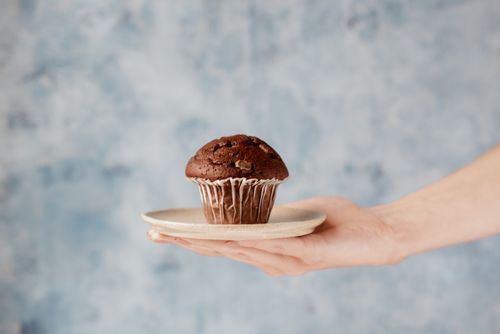 Free Crop anonymous female demonstrating small domed delicious baked chocolate muffin on ceramic plate Stock Photo