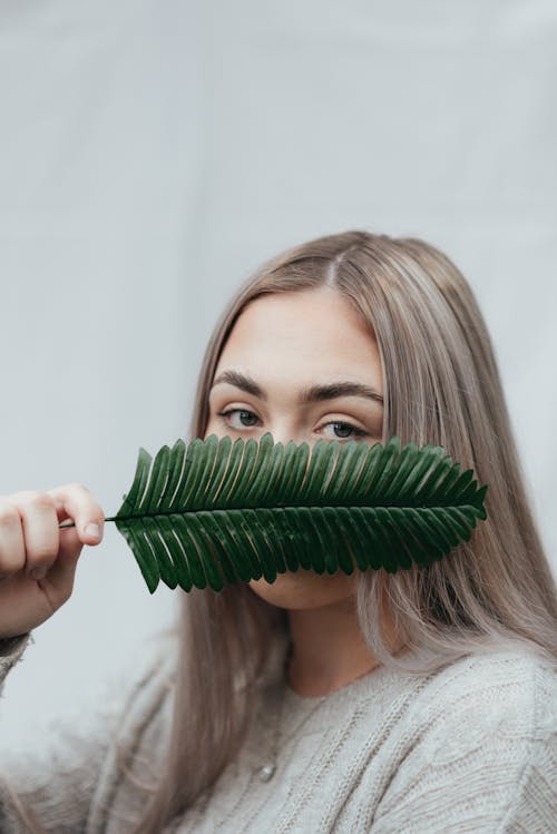 Woman covering face with green leaf