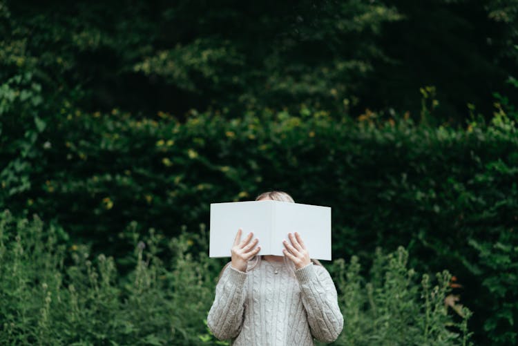 Woman Covering Face While Reading Book In Nature