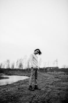 一个年轻人若有所思地站在乡村河岸边，穿着黑白衣服