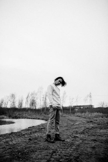 Black and white full body of serious young male standing on shore of river in countryside