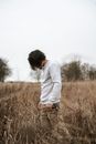 在宁静的乡村草地上，年轻人摆出沉思的姿势，周围环绕着高高的草丛
