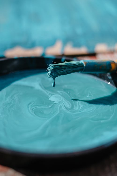 Free Azure paint dripping from paintbrush in bowl with stains placed near colorful cardboard in street with blurred background in sunlight Stock Photo
