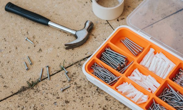 Handyman โ Top view of assorted repair instruments and screws in box near hammer and scotch tape on dirty tile in soft daylight