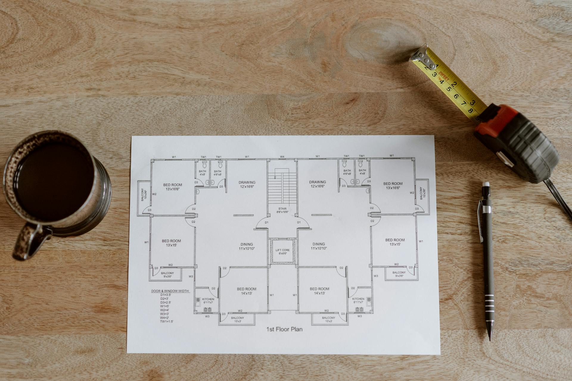 Top view of a floor plan with coffee, pen, and measuring tape on a wooden table.