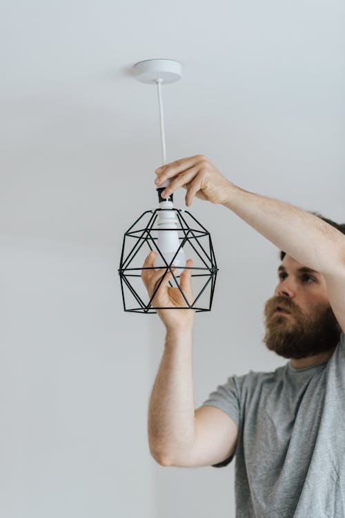 Concentrated repairman screwing light bulb in stylish lamp hanging on ceiling of new flat