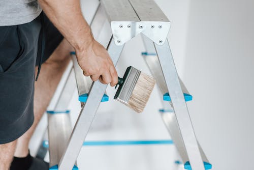 Free Painter with brush climbing ladder during renovation work Stock Photo