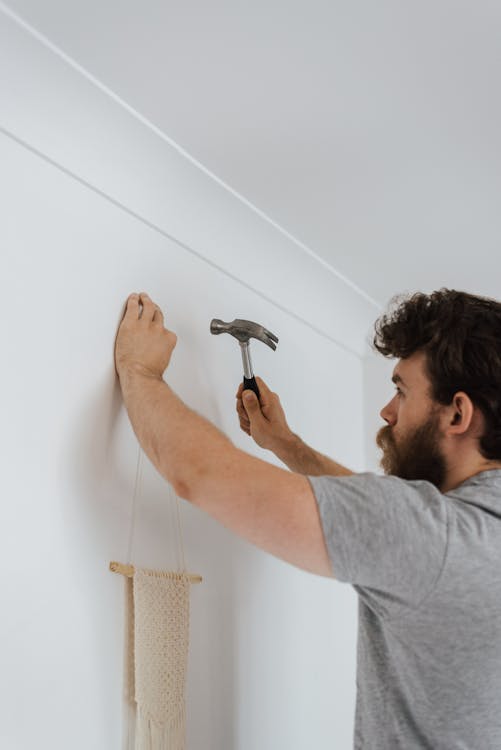 Man hammering nail into wall during housework · Free Stock Photo