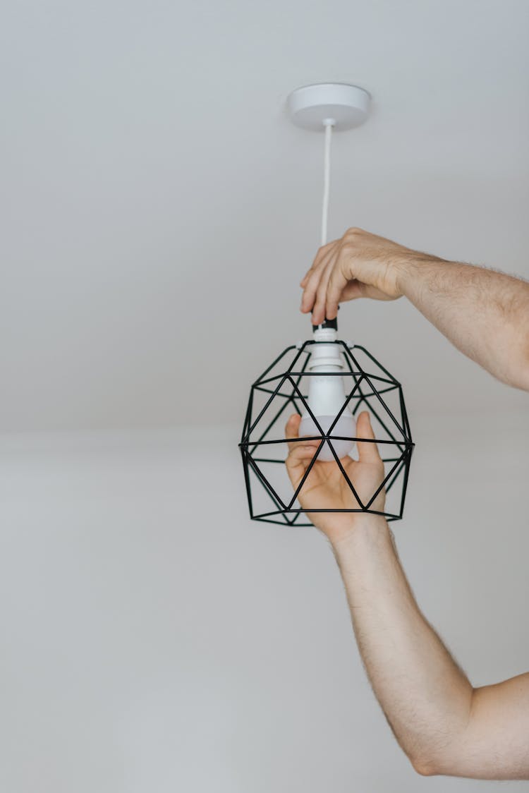 Crop Man Screwing Light Bulb Into Ornamental Lamp