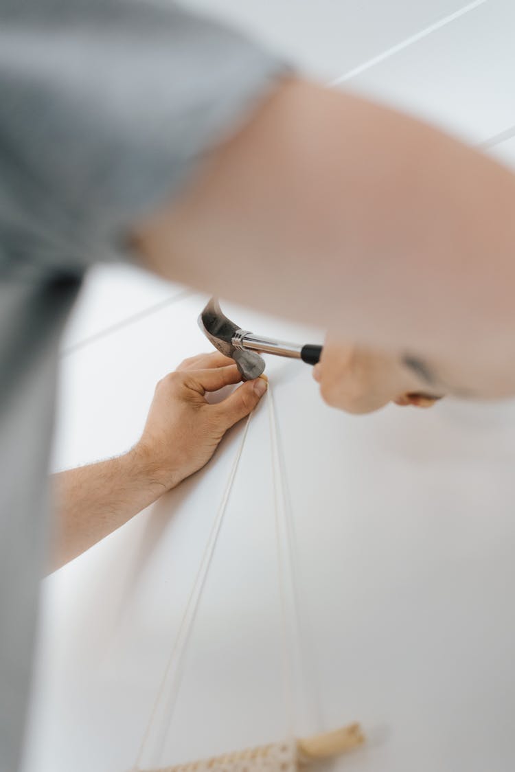 Faceless Man Putting Decoration On Wall While Using Hammer