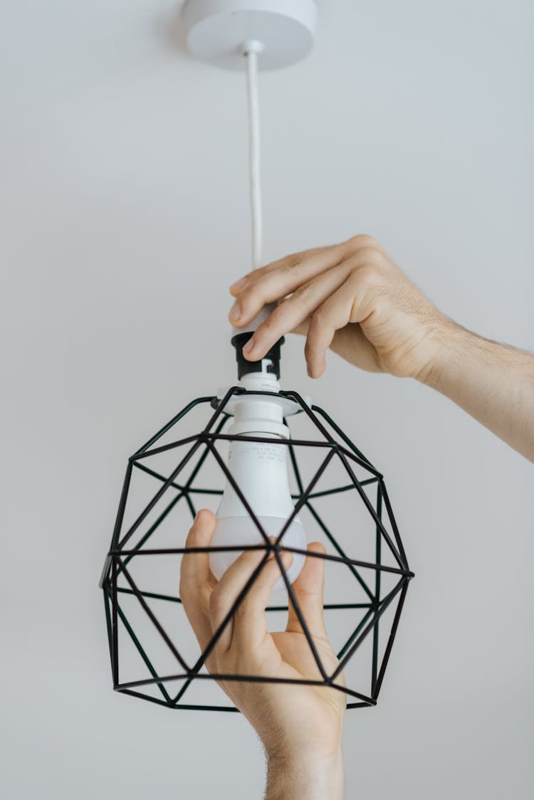 Faceless Man Screwing Bulb Into Metal Lamp At Home