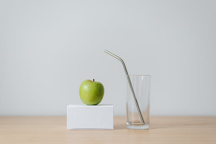 Green Apple On Box Near Empty Glass With Straw