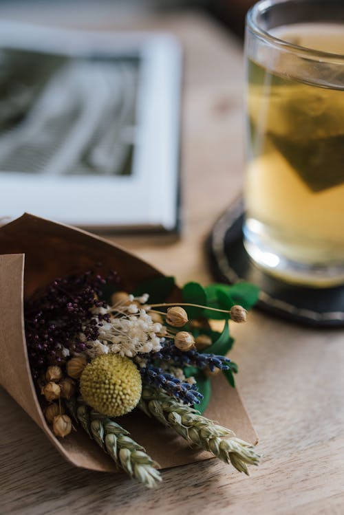 Small fragrant bouquet of fresh wildflowers placed on table with glass cup of herbal hot tea