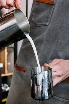 A professional barista pouring milk into a pitcher in a café setting, showcasing expertise.