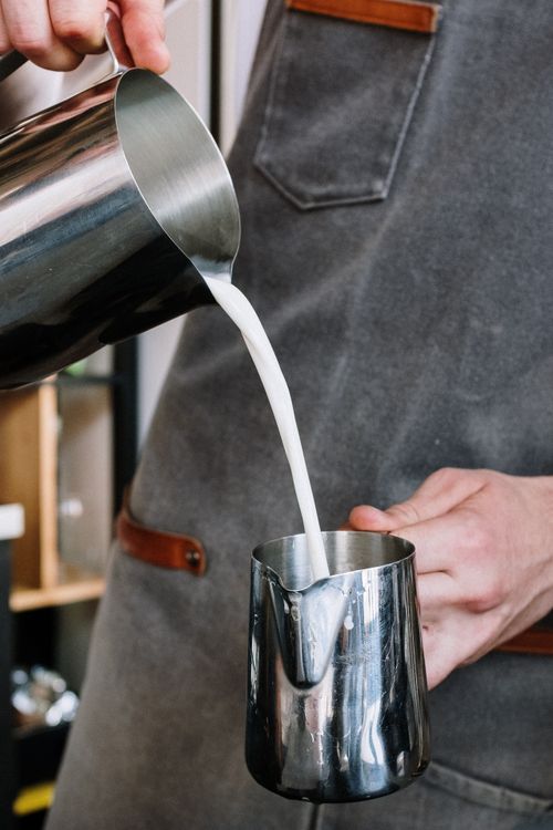 Free A professional barista pouring milk into a pitcher in a café setting, showcasing expertise. Stock Photo