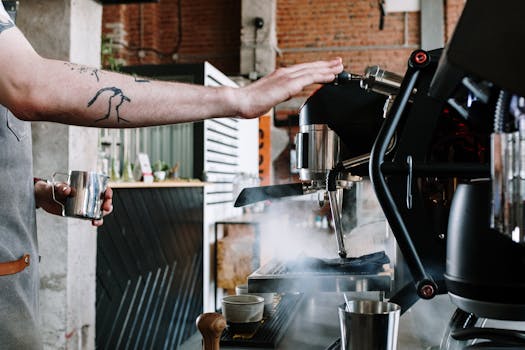 Close-up of a barista steaming milk at a coffee house with an espresso machine.