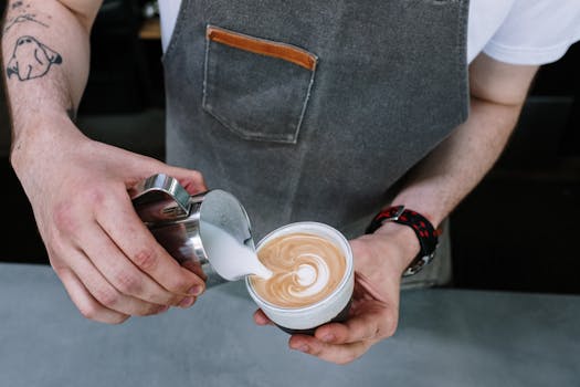 Close-up of a barista creating latte art with milk in a coffee shop.
