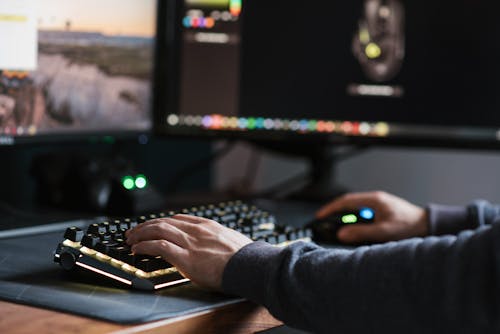 Crop anonymous male in casual outfit working on modern computer and typing on keyboard at home