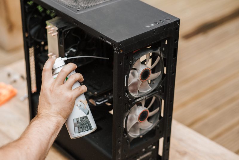 A person using compressed air to remove dust from computer components