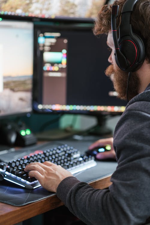 Free Side view crop focused bearded male wearing headset browsing modern computer while typing on keyboard Stock Photo