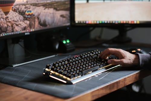 Free Crop anonymous male using contemporary computer with big monitors and typing on backlit keyboard Stock Photo