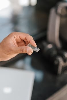 A close-up shot of a hand holding a USB flash drive over a blurred office desk.