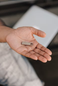 A person holding a modern metallic USB flash drive in their palm against a blurred background.