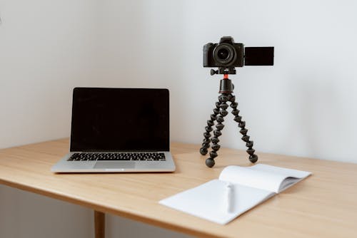 Free Modern workplace consisting of netbook camera on tripod near opened planner with pen on wooden table Stock Photo