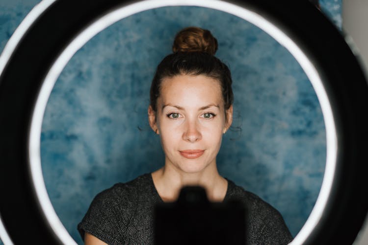 Young Content Woman Taking Selfie In Light Of Studio Lamp