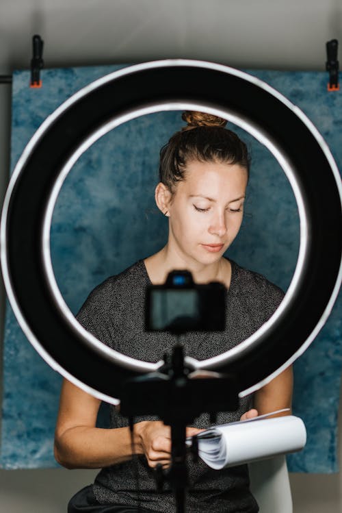 Free Young female examining notes in notebook in professional studio with photo camera and studio lamp Stock Photo