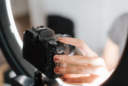 Crop anonymous female with neat manicure configuring modern photo camera near studio lamp in soft focus