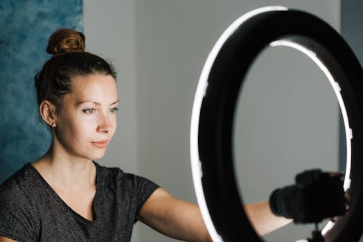 Young female in casual T shirt taking selfie with digital photo camera near professional studio lamp
