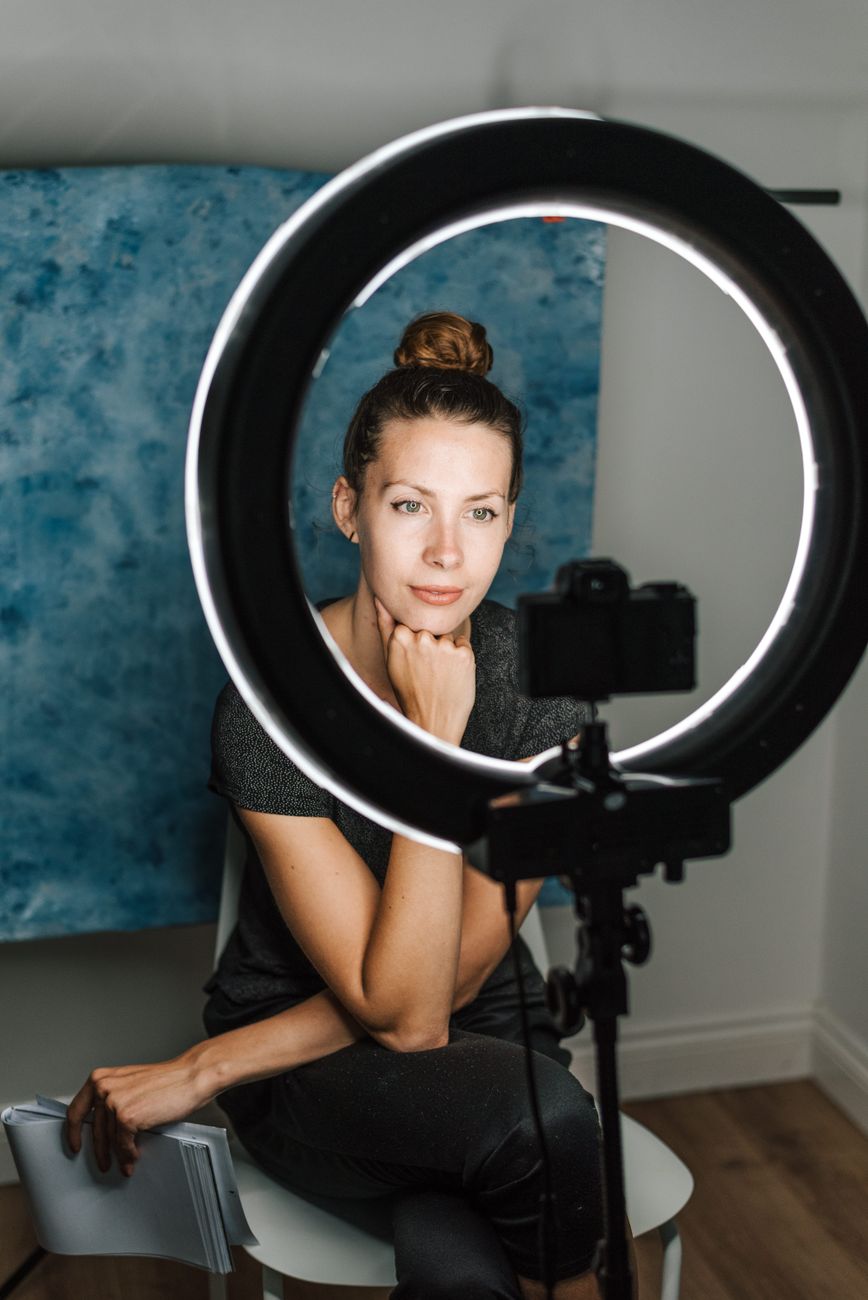 Young female taking selfie with contemporary photo camera and bright round studio lamp