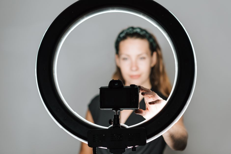 Young female taking self portrait with modern photo camera and studio lamp on white background
