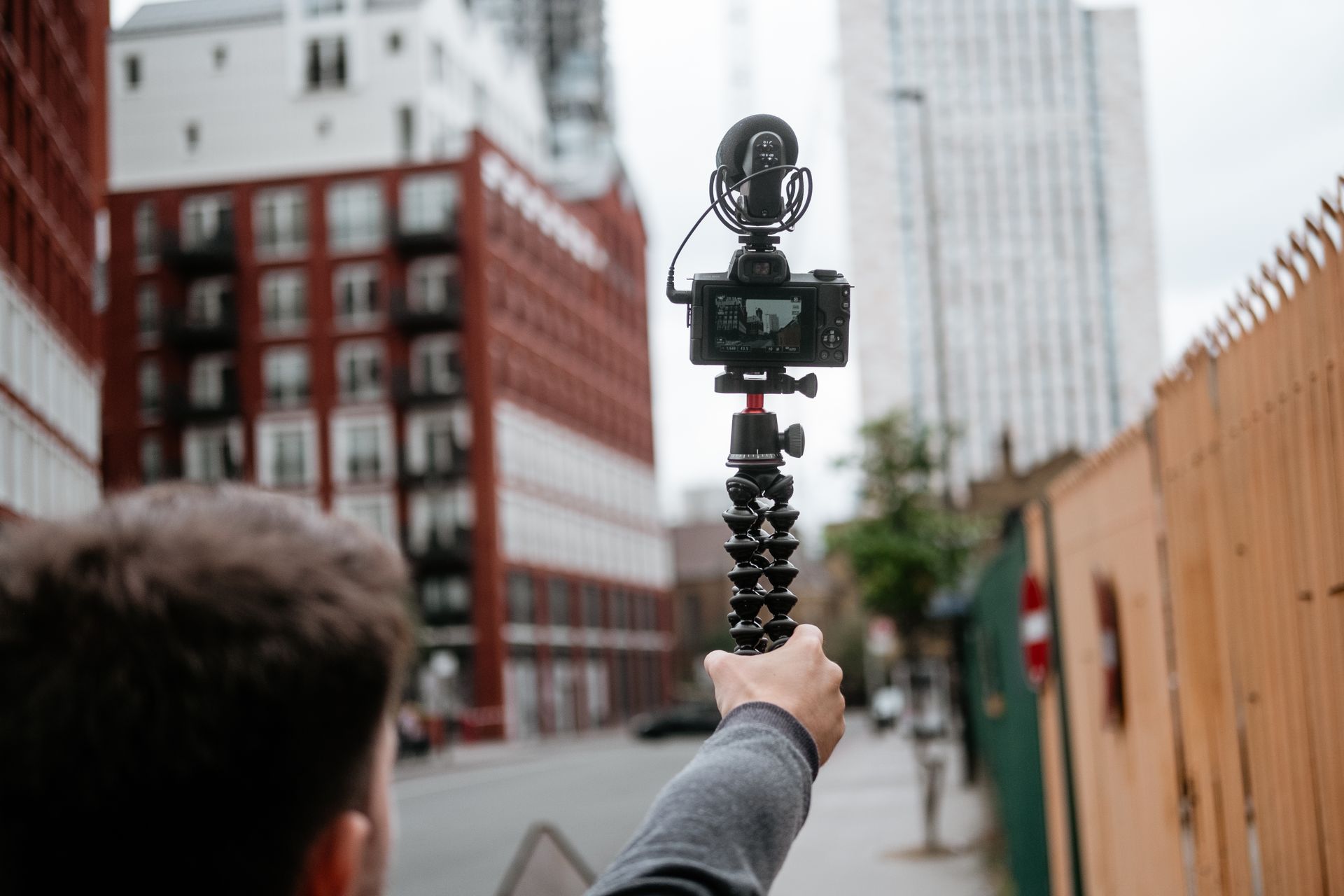 Crop anonymous male recording video of town with modern buildings with digital photo camera in soft focus
