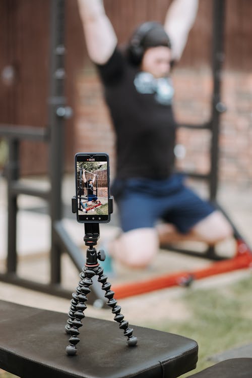 Sporty trainer recording video of workout on horizontal bar with smartphone in soft focus