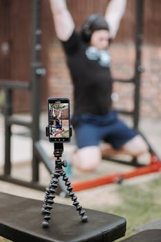 Sporty trainer recording video of workout on horizontal bar with smartphone in soft focus