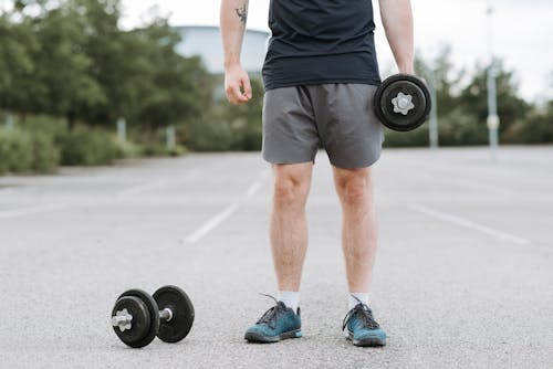 Crop unrecognizable male with great stamina lifting heavy dumbbells while doing exercises alone on paved ground