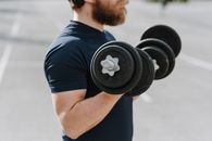 Side view of crop male in t shirt doing bicep curls with dumbbells training on sports ground