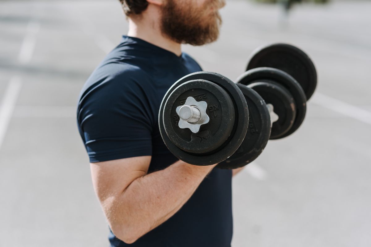 Muscular man doing exercise with dumbbells in an urban outdoor setting