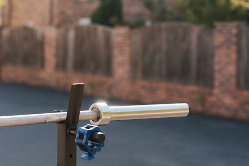 Part of steel barbell without weight discs for training on stand against fence in sunlight